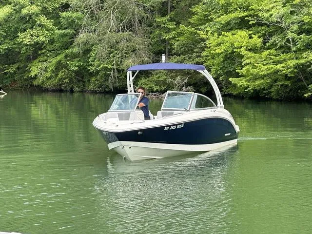 Slide: The Image of 2023 Chaparral 23 SSi boat cruising on a serene, green lake surrounded by lush trees. - 8