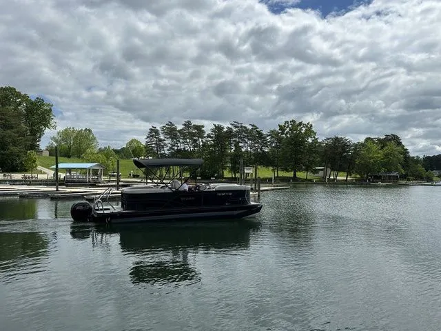 Slide: The Image of 2023 Sylvan Mirage X3 pontoon boat on a serene lake with cloudy skies. - 6