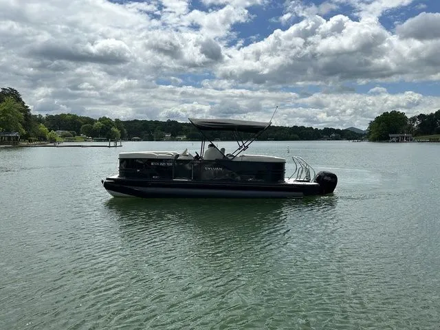 Slide: The Image of 2023 Sylvan Mirage X3 pontoon boat on a serene lake under a cloudy sky. - 7