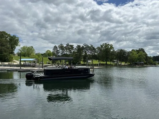 Slide: The Image of 2023 Sylvan Mirage X3 pontoon boat on a serene lake under a cloudy sky. - 6