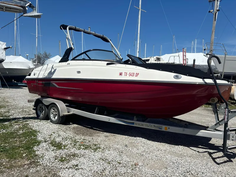 The Image of 2016 Bayliner 215 Deck Boat on trailer, red and white, parked outdoors. - 0