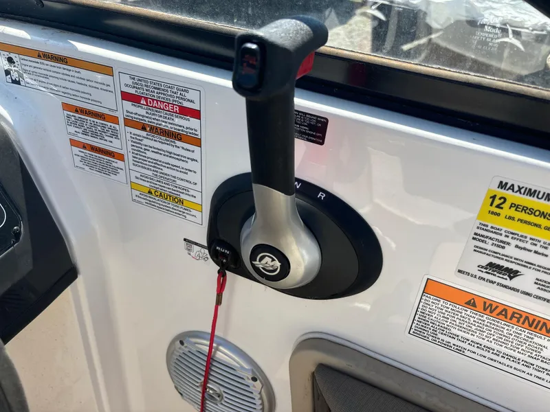 Slide: The Image of Throttle control of 2016 Bayliner 215 Deck Boat with safety warnings and capacity label. - 16