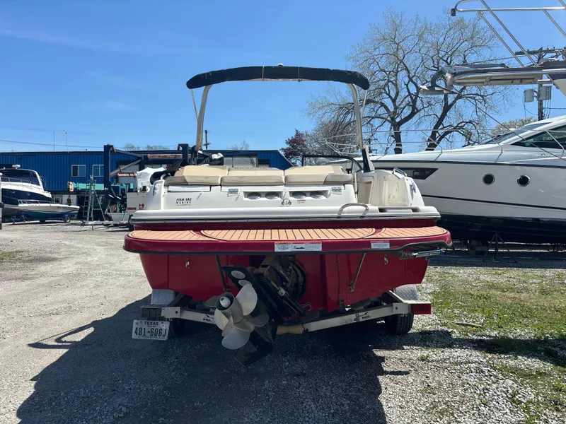 Slide: The Image of 2016 Bayliner 215 Deck Boat with red hull, parked on a trailer in a marina. - 2
