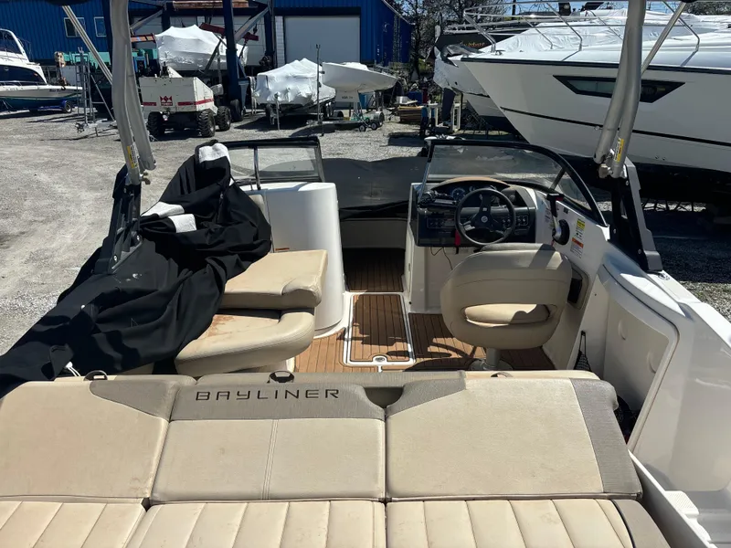 Slide: The Image of 2016 Bayliner 215 Deck Boat interior with seating and steering wheel, docked outdoors. - 8