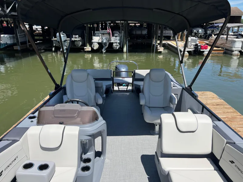 Slide: The Image of 2025 Starcraft GX 22 R DH Sport boat interior with seating and canopy, docked at marina. - 6