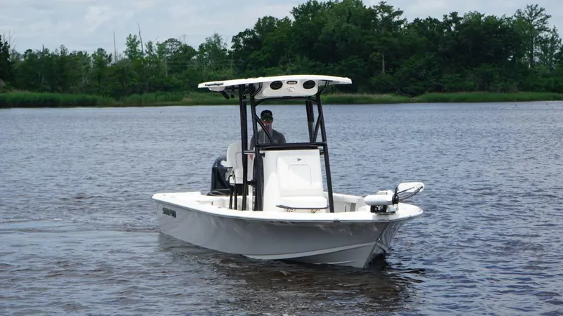 Slide: The Image of 2024 Sea Pro 230 Bay boat cruising on a calm lake with lush green trees. - 2