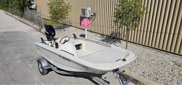Slide: The Image of 2012 Boston Whaler SPORT 130 boat on trailer, parked near a building. - 1