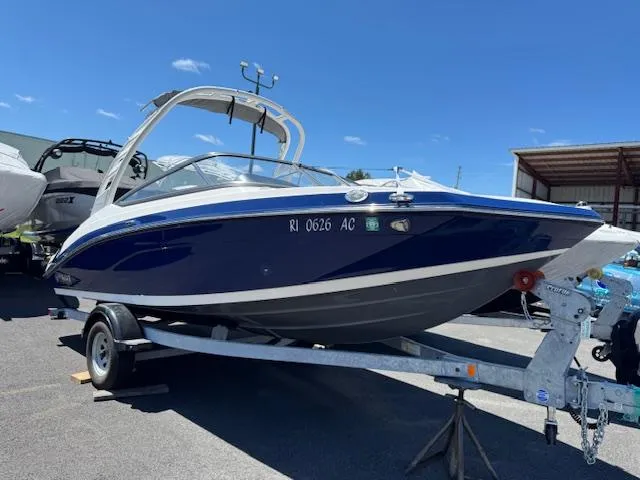 Slide: The Image of 2021 Yamaha Boats 195S on trailer, blue and white, parked outdoors under clear sky. - 0