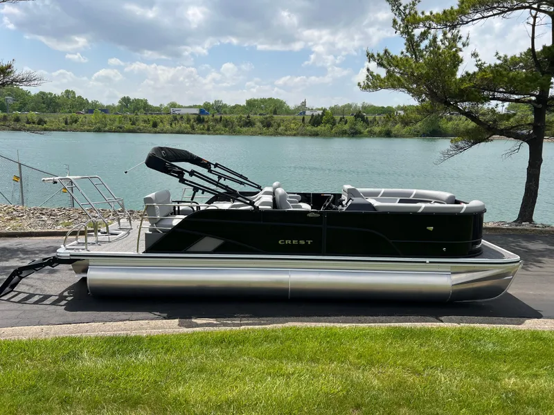 Slide: The Image of 2025 Crest Classic 220 SLRC pontoon boat by a serene lake under a partly cloudy sky. - 4
