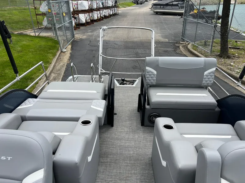 Slide: The Image of 2025 Crest Classic 220 SLRC pontoon boat with gray seating and cup holders, docked near a fence. - 12