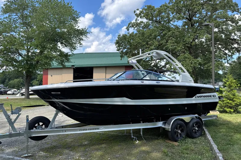 Slide: The Image of 2025 Chaparral 247 SSX boat on trailer, parked outdoors near trees and a building. - 2