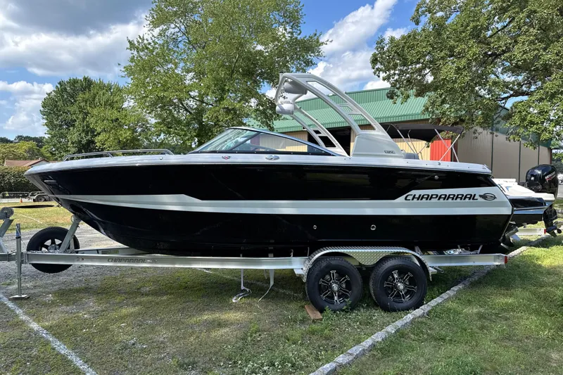 Slide: The Image of 2025 Chaparral 247 SSX boat on trailer, parked outdoors with trees and building in background. - 3