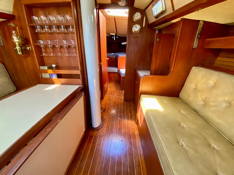 Slide: The Image of 1979 Valiant 37 yacht interior with wooden flooring, cushioned seating, and glassware display. - 35