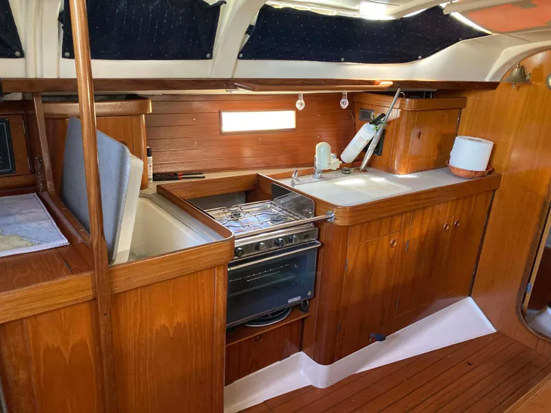 Slide: The Image of Interior of 1993 Beneteau Oceanis 370 yacht, featuring a wooden kitchen with stove and sink. - 13