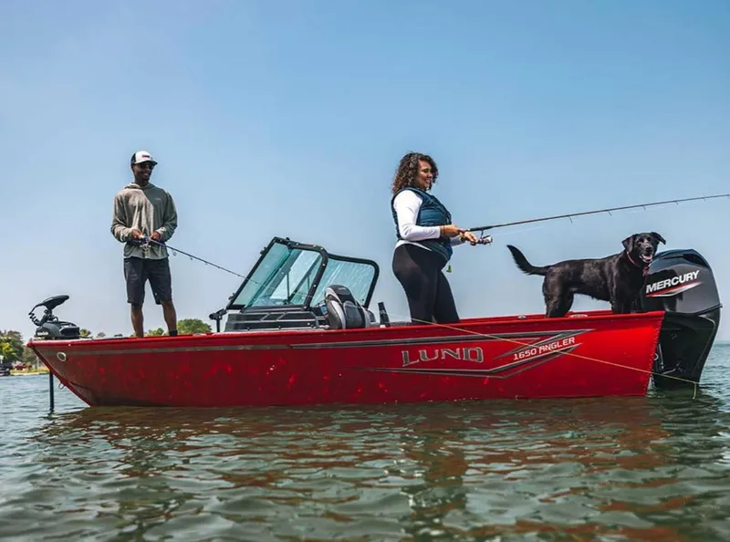 Slide: The Image of 2026 Lund 1650 Angler boat with two people and a dog fishing on a lake. - 0