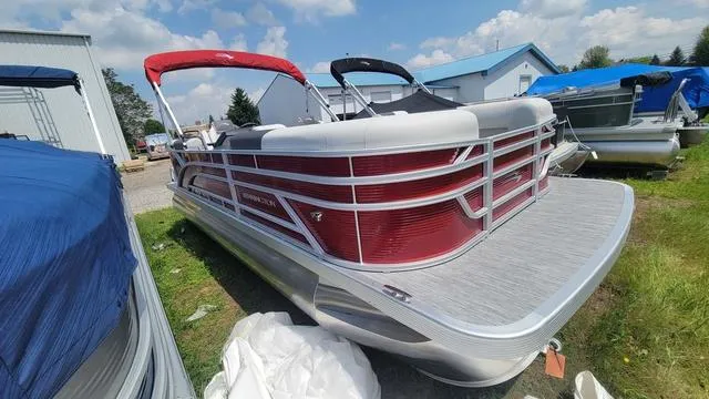 Slide: The Image of 2025 Bennington S Quad Bench 22 SSR pontoon boat with red accents, parked outdoors. - 11