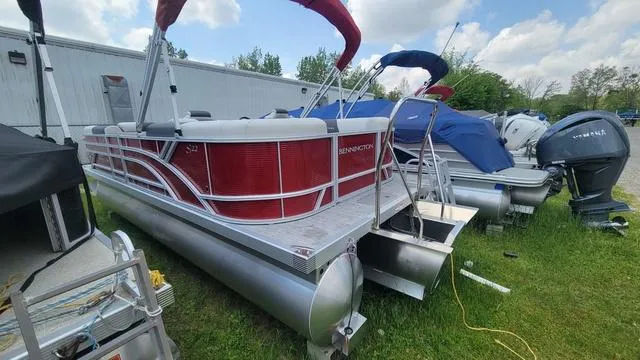 Slide: The Image of 2025 Bennington S Quad Bench 22 SSR pontoon boat with red accents, docked outdoors. - 9