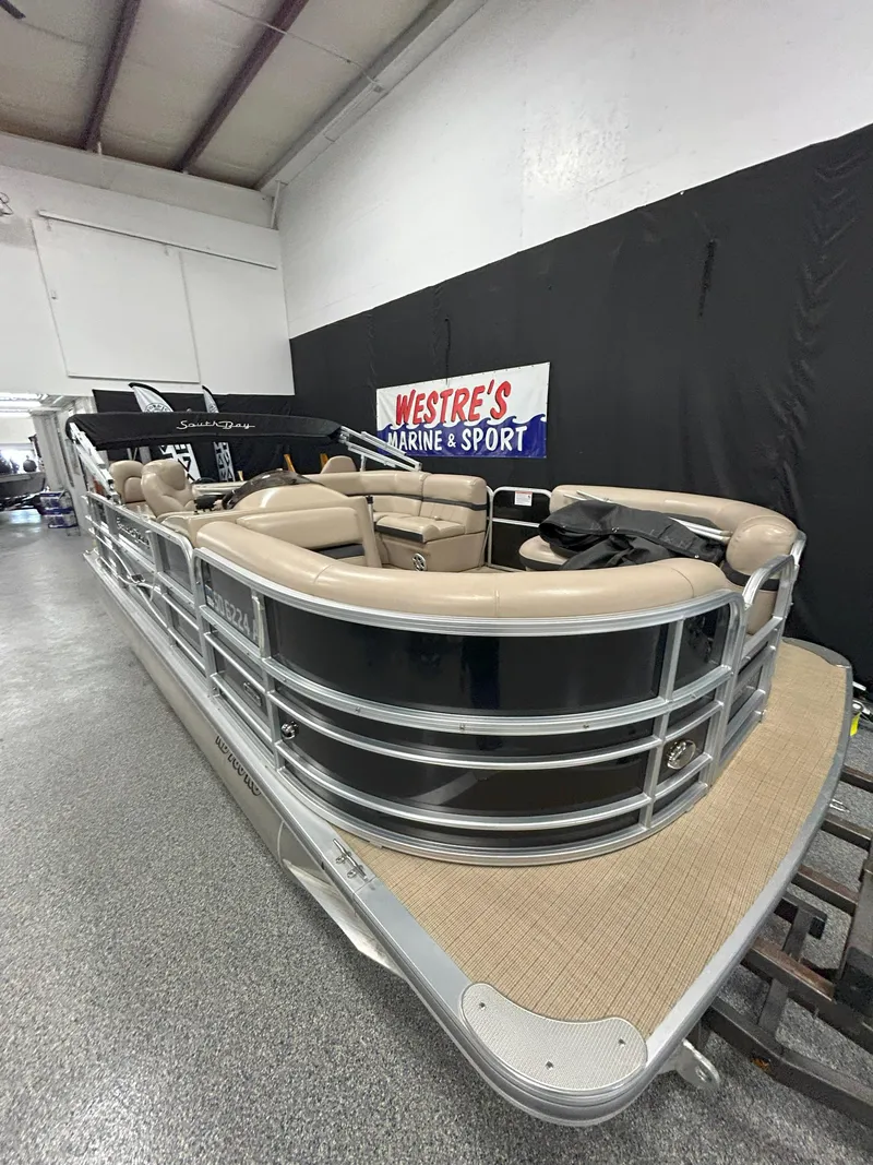 Slide: The Image of 2018 South Bay 220FCR pontoon boat in showroom, beige seating, Westre's Marine & Sport sign. - 2