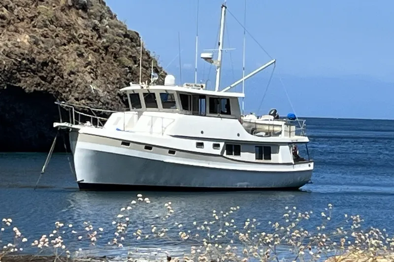 The Image of Kadey-Krogen 48 Whaleback 1996 yacht anchored near rocky coastline, clear blue water. - 0