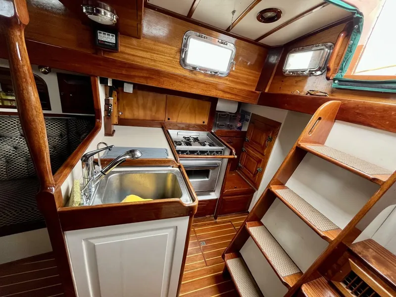Slide: The Image of 1979 Cherubini 44 yacht interior with wooden cabinetry, compact kitchen, and stainless steel sink. - 11