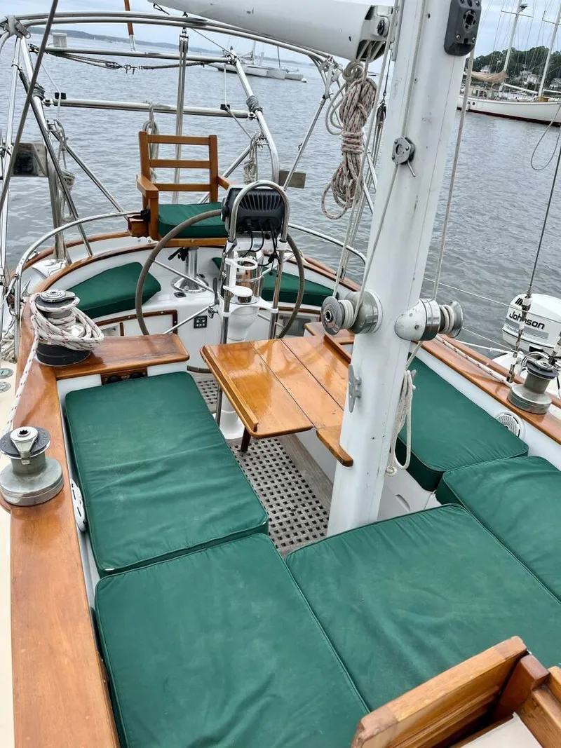 Slide: The Image of 1979 Cherubini 44 sailboat cockpit with green cushions and wooden accents, docked at a marina. - 2