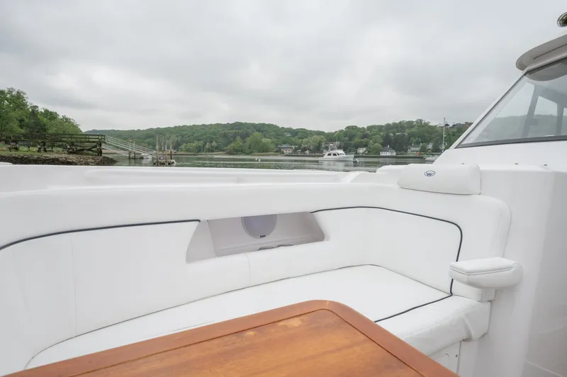 Slide: The Image of 2021 Southport 33 DC boat with white seating and wooden table, docked by a scenic riverside. - 24