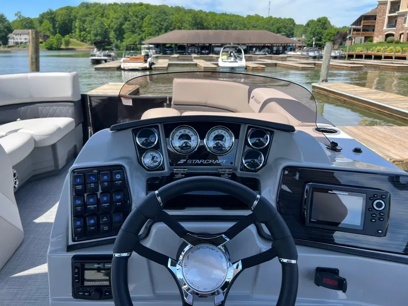 Slide: The Image of 2025 Starcraft SLS 3 boat dashboard with steering wheel, gauges, and navigation system at a marina. - 7