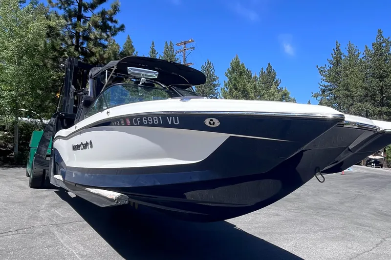 Slide: The Image of 2022 MasterCraft X26 boat on trailer, surrounded by trees and clear blue sky. - 2