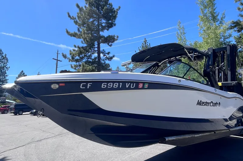 Slide: The Image of 2022 MasterCraft X26 boat on trailer, parked outdoors under clear blue sky. - 3