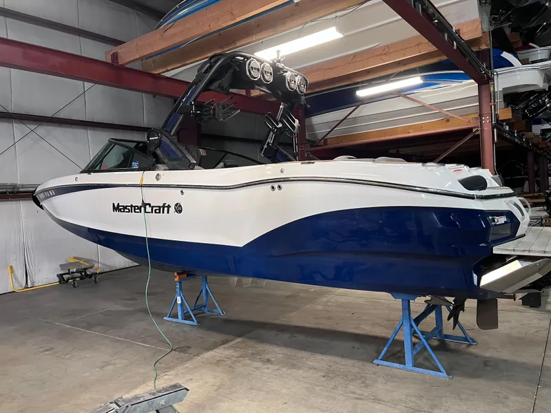 Slide: The Image of 2022 MasterCraft X26 boat in a garage on stands, blue and white design. - 5
