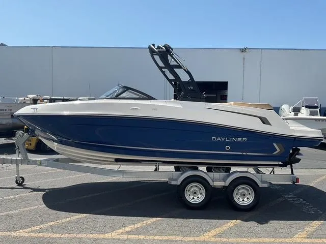 Slide: The Image of 2025 Bayliner VR5 Bowrider I/O on trailer, blue and white design, parked outdoors. - 4