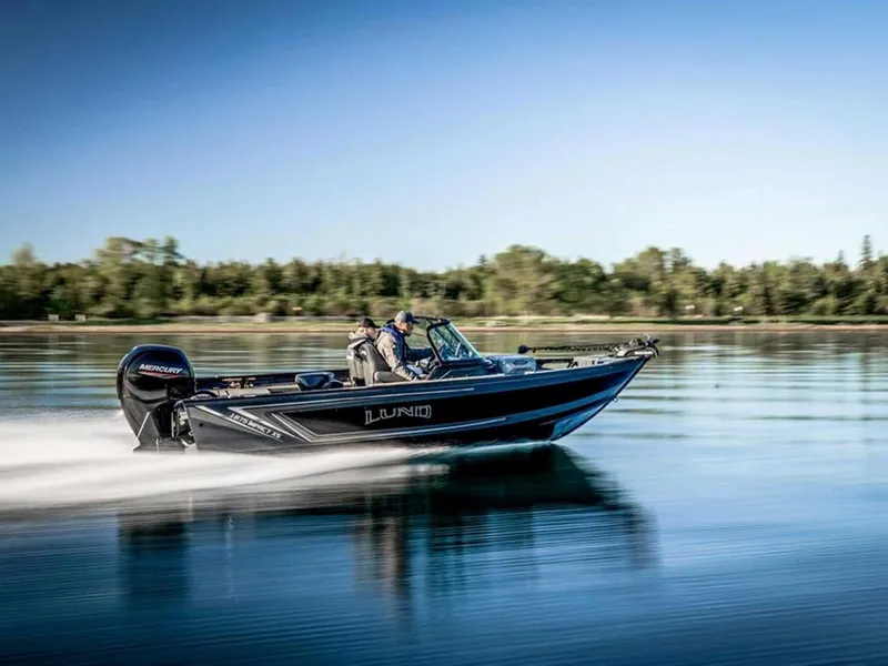 Slide: The Image of 2026 Lund 1875 Impact XS boat speeding on a calm lake with trees in the background. - 11