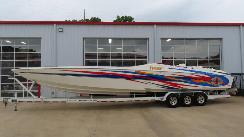 Slide: The Image of 2004 Cigarette 42 Tiger speedboat with vibrant graphics on a trailer outside a garage. - 0