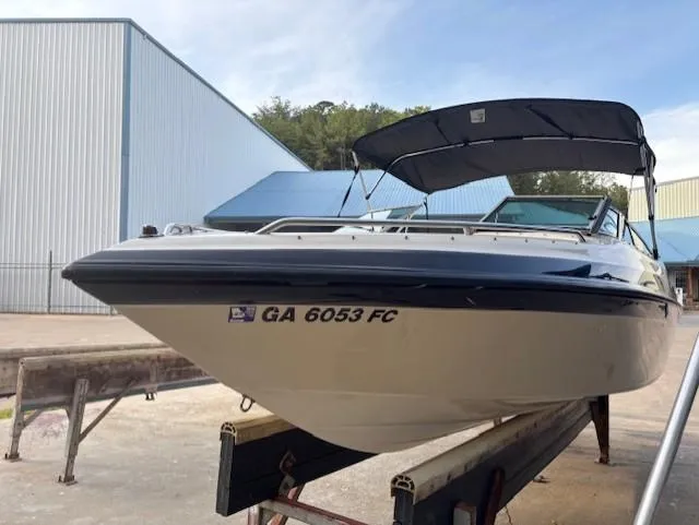 Slide: The Image of 1999 Crownline 202 boat on trailer, with canopy, parked near industrial buildings. - 3