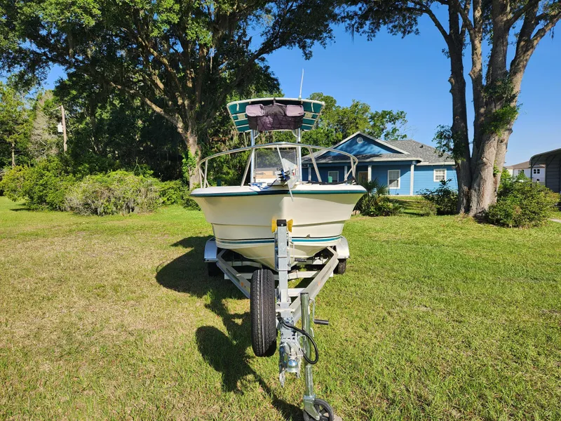 Slide: The Image of 2005 Key Largo 210 CC boat on trailer, parked on grass with trees and house in background. - 2
