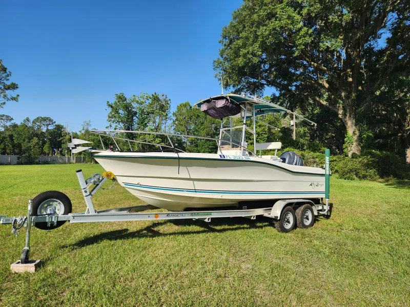 Slide: The Image of 2005 Key Largo 210 CC boat on trailer, parked on grassy field with trees in background. - 3