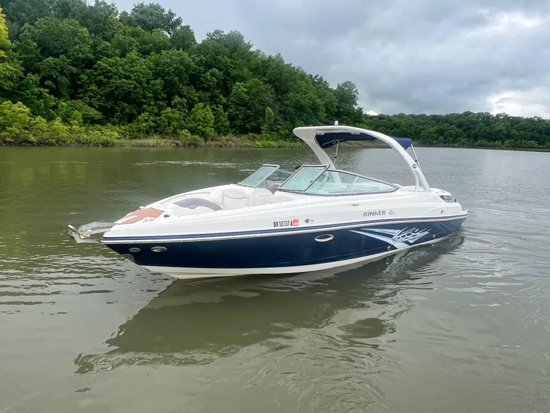 Slide: The Image of 2011 Rinker 276 Captiva Bowrider on calm lake with lush green forest backdrop. - 6