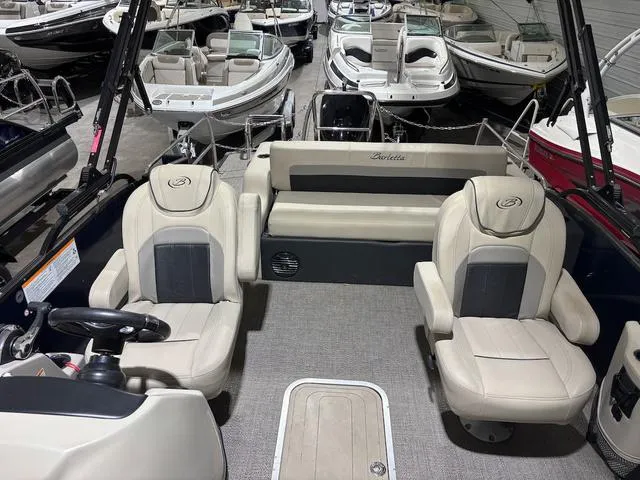 Slide: The Image of 2021 Barletta Boats C24uc interior with beige seating, surrounded by other boats in a showroom. - 4