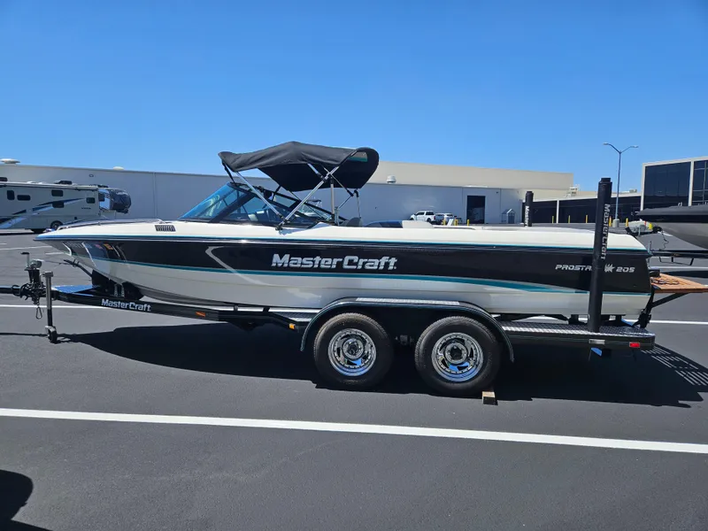 Slide: The Image of 1992 MasterCraft Prostar 205 boat on trailer, parked in a lot under clear blue sky. - 3