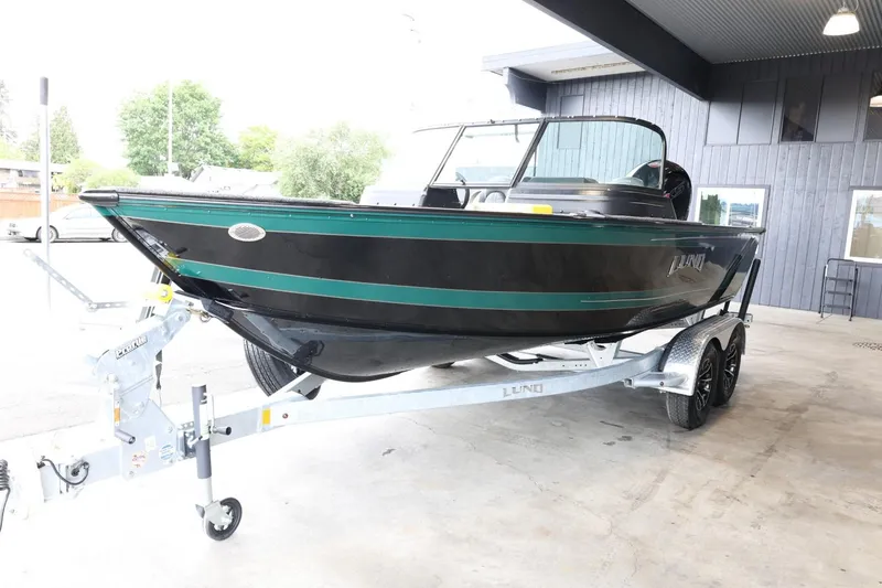 Slide: The Image of 2025 Lund 1875 Impact XS Sport boat on trailer, black and green exterior, parked indoors. - 4