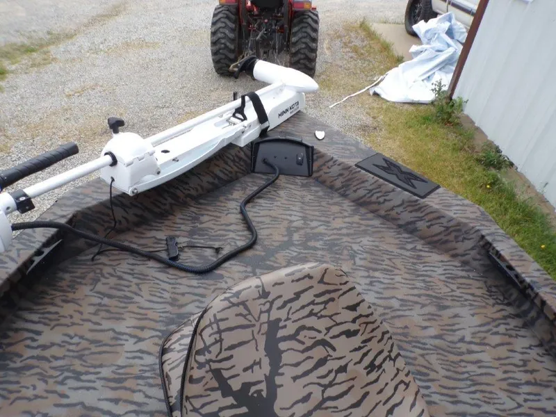 Slide: The Image of 2025 Xpress H20BAY boat with camouflage interior and trolling motor, parked near a tractor. - 12