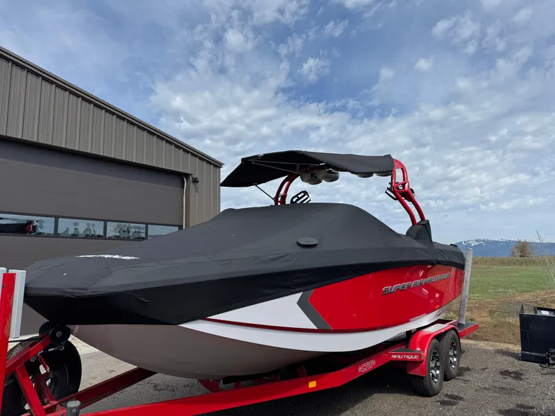 Slide: The Image of 2014 Correct Craft G23 boat with cover on red trailer, parked near a building. - 6