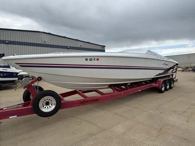 Slide: The Image of 2000 Baja 36 Outlaw speedboat on red trailer, parked outdoors near warehouse. - 2