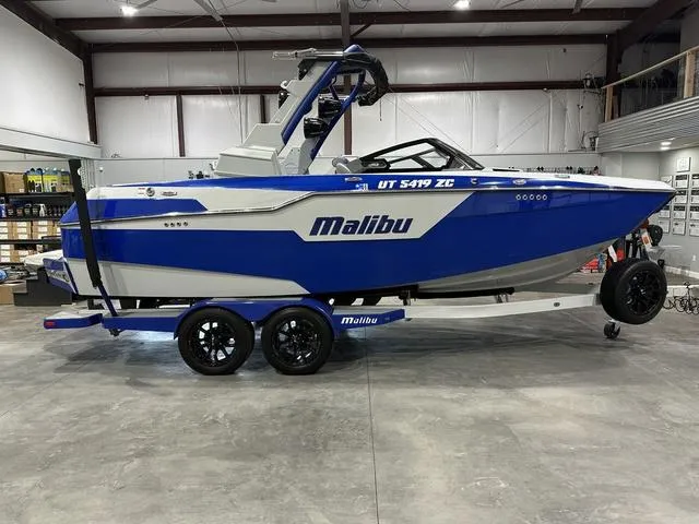 Slide: The Image of 2021 Malibu M220 boat in blue and white, parked indoors on a trailer. - 1