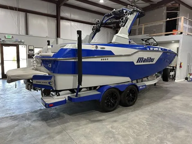 Slide: The Image of 2021 Malibu M220 boat in a garage, featuring a blue and white design on a trailer. - 2