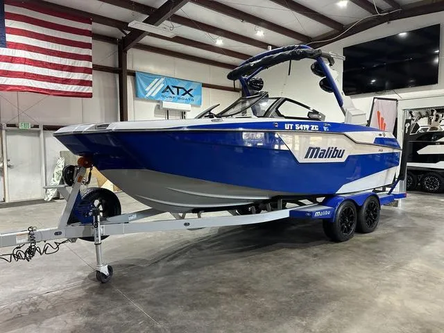 Slide: The Image of 2021 Malibu M220 boat in showroom, blue and white design, on trailer. - 5