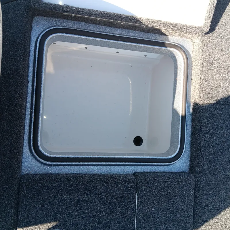 Slide: The Image of 2025 Ranger Z185 boat storage compartment with carpeted edges and drainage hole. - 13