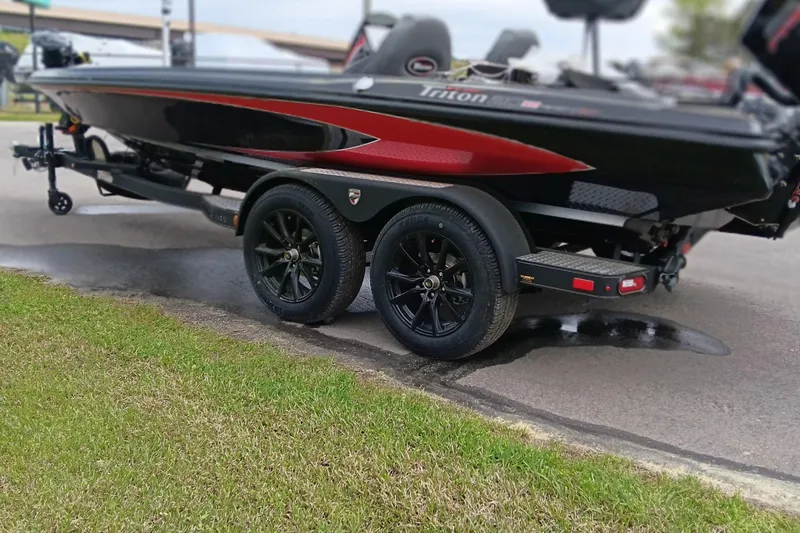 Slide: The Image of 2025 Triton 20XP Patriot boat on trailer, black and red design, parked on grass. - 2