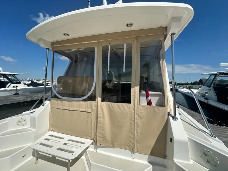Slide: The Image of 2013 Back Cove 34 boat with beige canopy and seating, docked under a clear blue sky. - 33