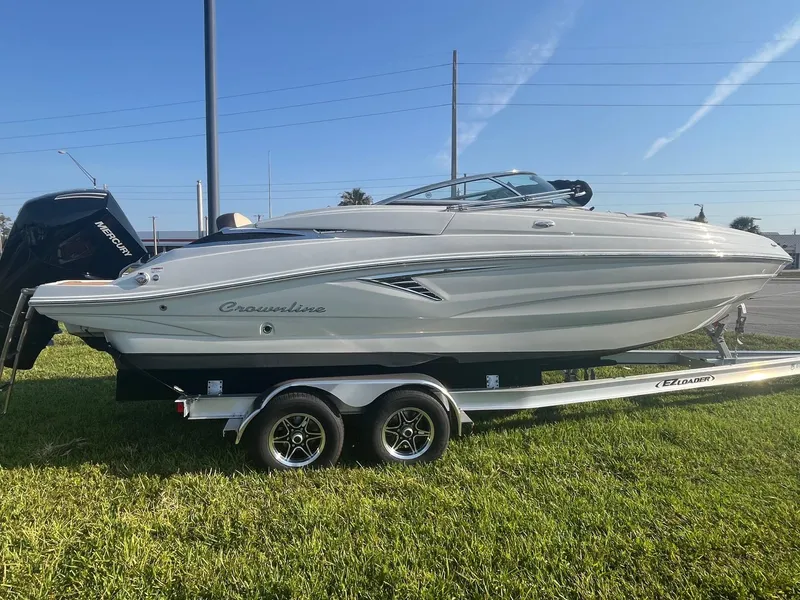 The Image of 2022 Crownline 260 XSS boat on trailer, parked on grass under clear blue sky. - 0